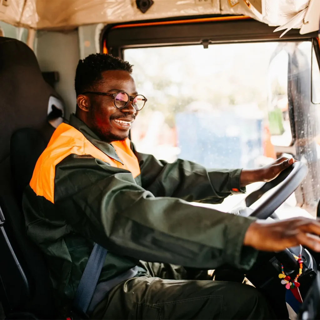 Young African American garbage removal worker driving a waste truck.