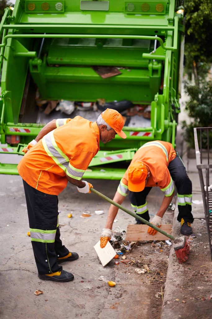 Two junk removal experts, young and old, sweep and clean up a street.