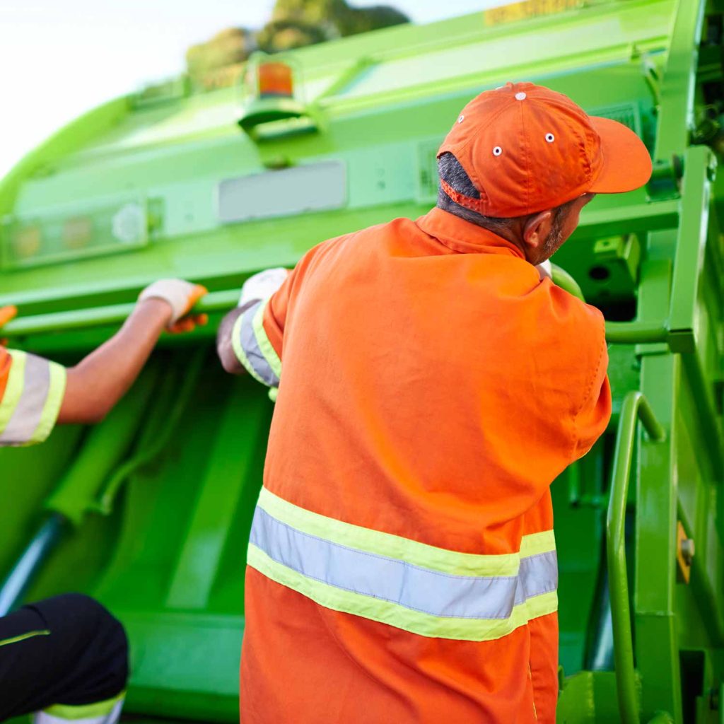 Close up behind a trash removal expert standing behind a lime green garbage truck.