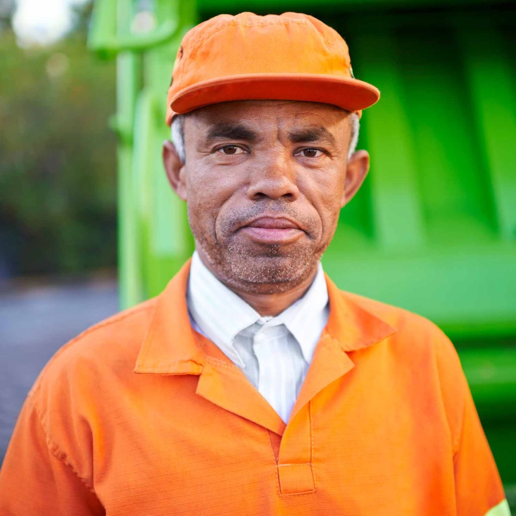 Close up of a trash removal expert in front of a lime green garbage truck.