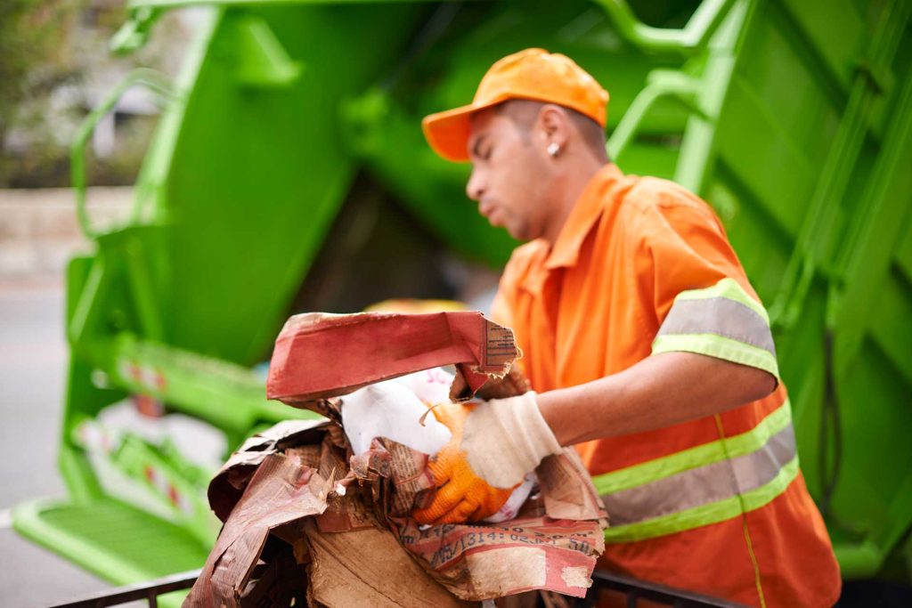 A junk removal expert picks up trash and throws it in the back of a garbage truck.